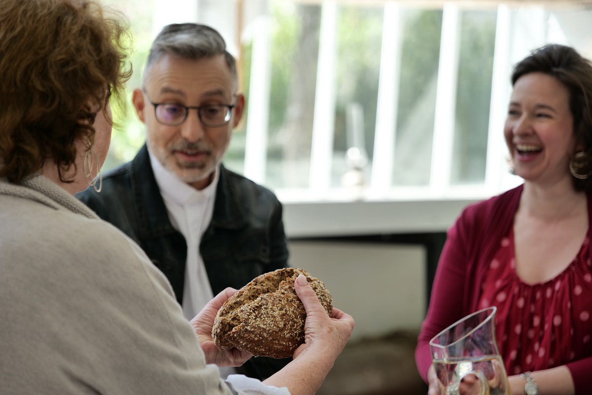 © @no-te.com/S.Cucui Drei Menschen sitzen beisammen und teilen Brot.